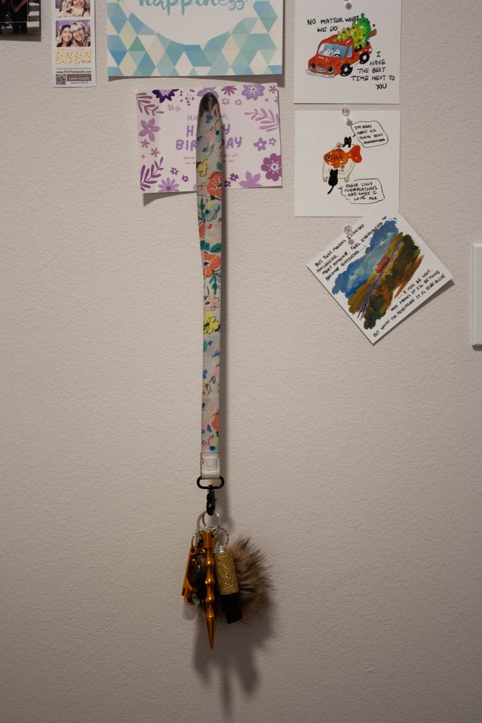 A lanyard hanging on a decorated wall with pepper spray, a window breaker, and other items