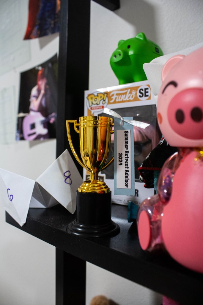 A shelf of items surrounding a miniature trophy with a "Summer Retreat Advisor 2024" tag attached to it