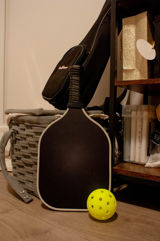 A pickleball paddle and ball resting on the edge of a basket and shelving structure