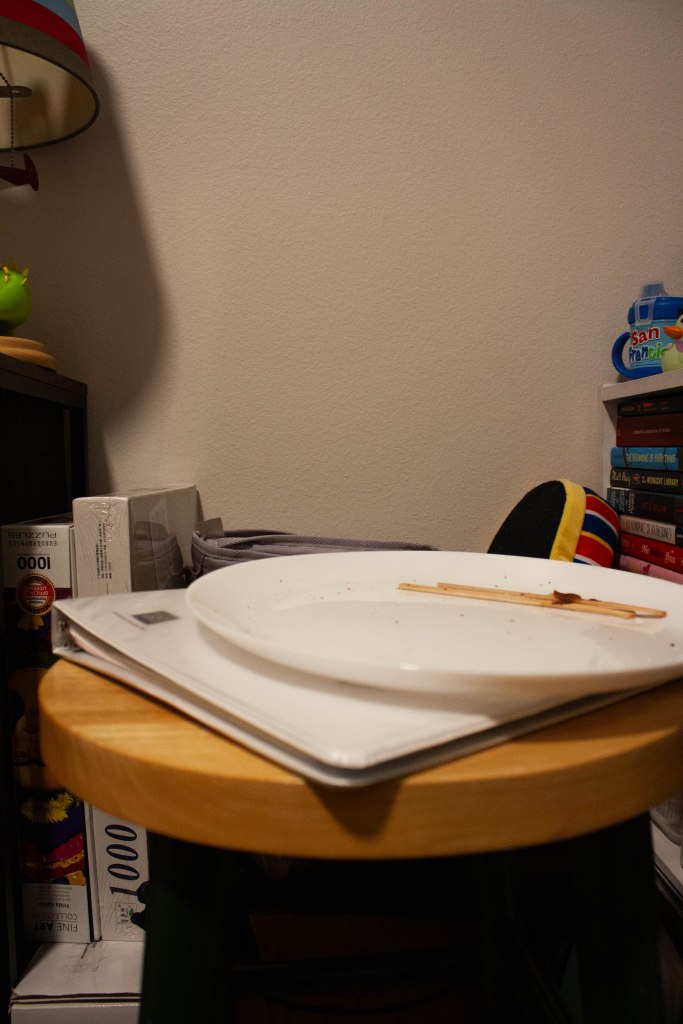 An empty, used plate resting on top of a binder and stool surrounded by background items